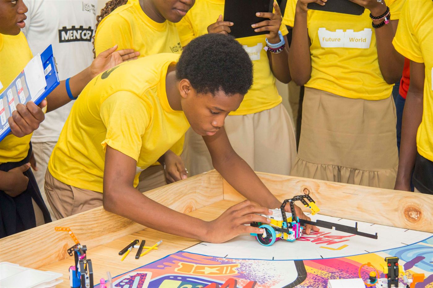 Un élève en t-shirt jaune place son robot LEGO sur la table de jeu