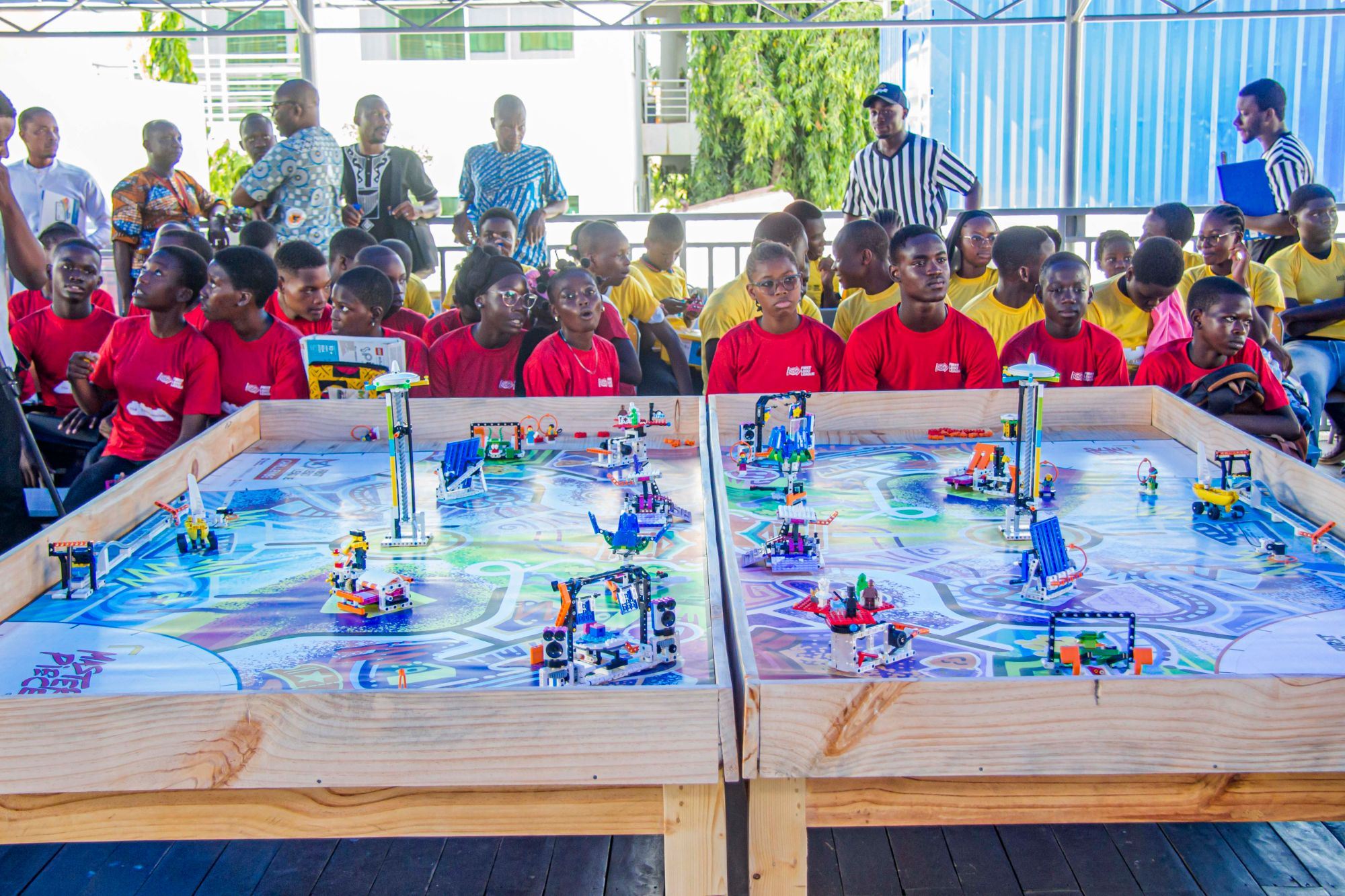 Deux tables de jeu FIRST LEGO League MASTERPIECE, avec les équipes en t-shirts rouges et jaunes derrière