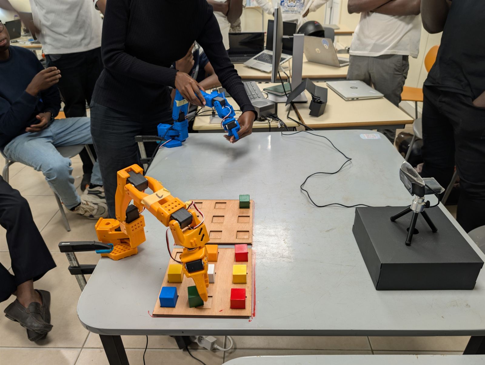 Téléopération : le bras leader bleu guide le bras follower orange au-dessus d'un plateau de cubes