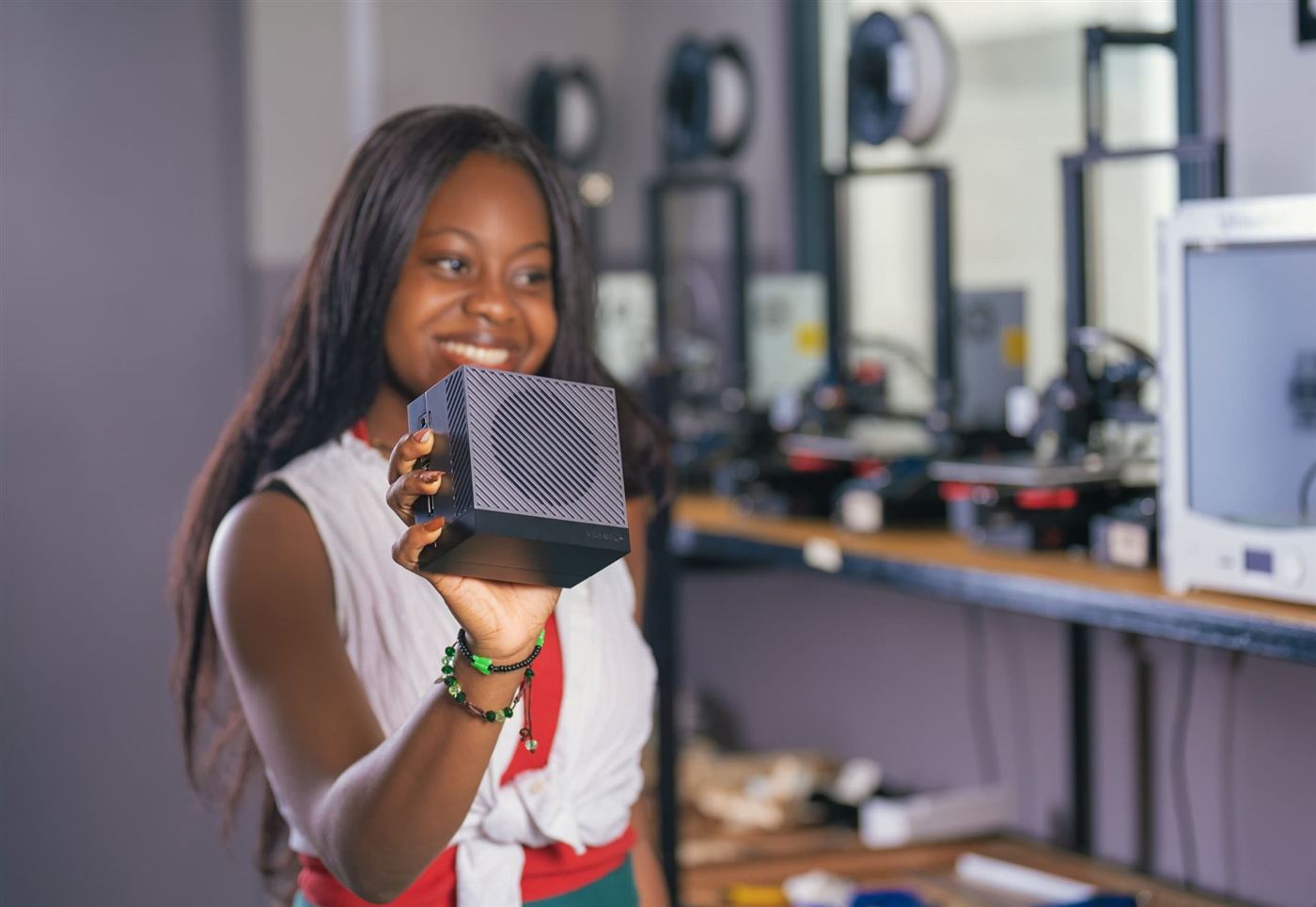 Une apprenante présente un mini-ordinateur devant des imprimantes 3D